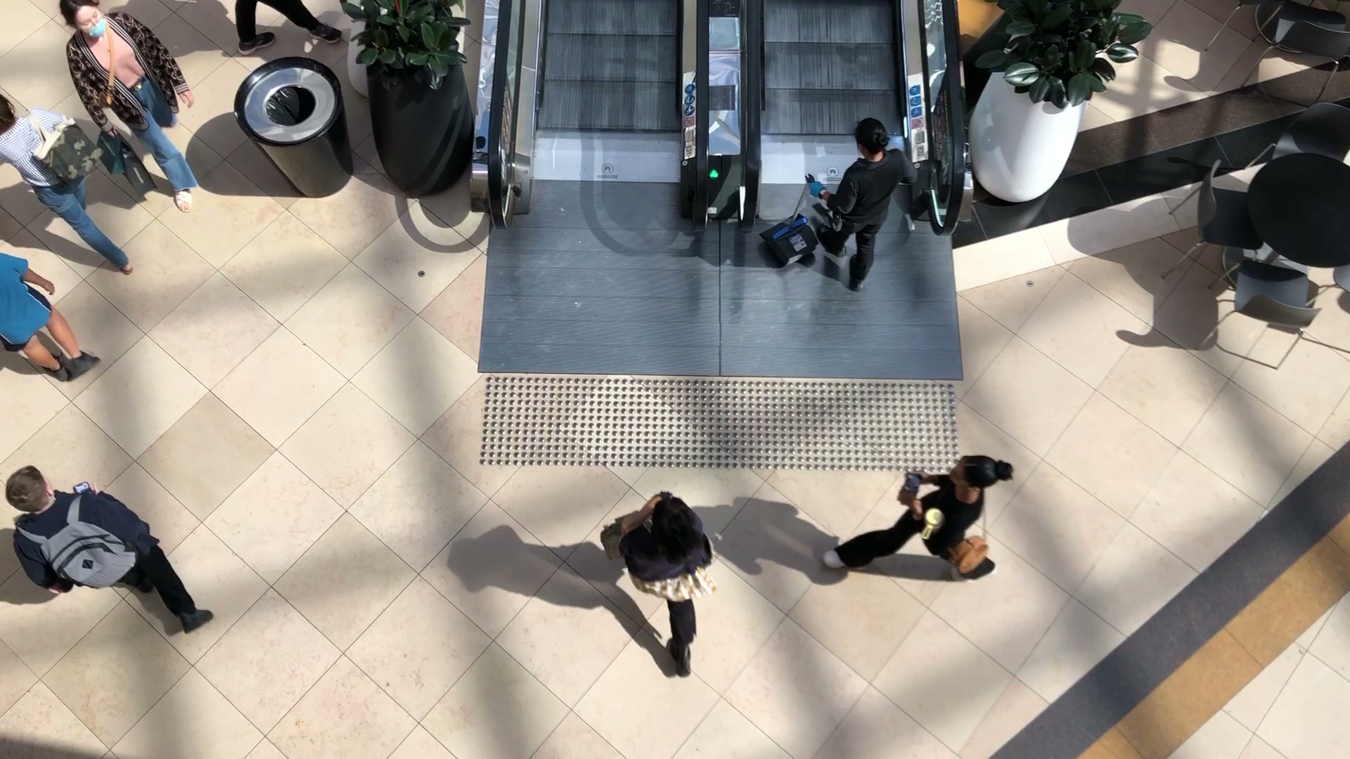 Overhead retail scene with shoppers moving near an escalator
